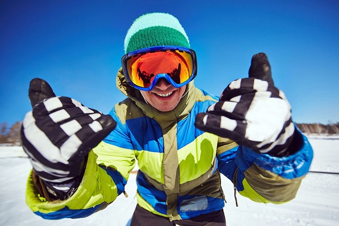 Young snowboarder in sportswear looking through protective eyeglasses at winter resort